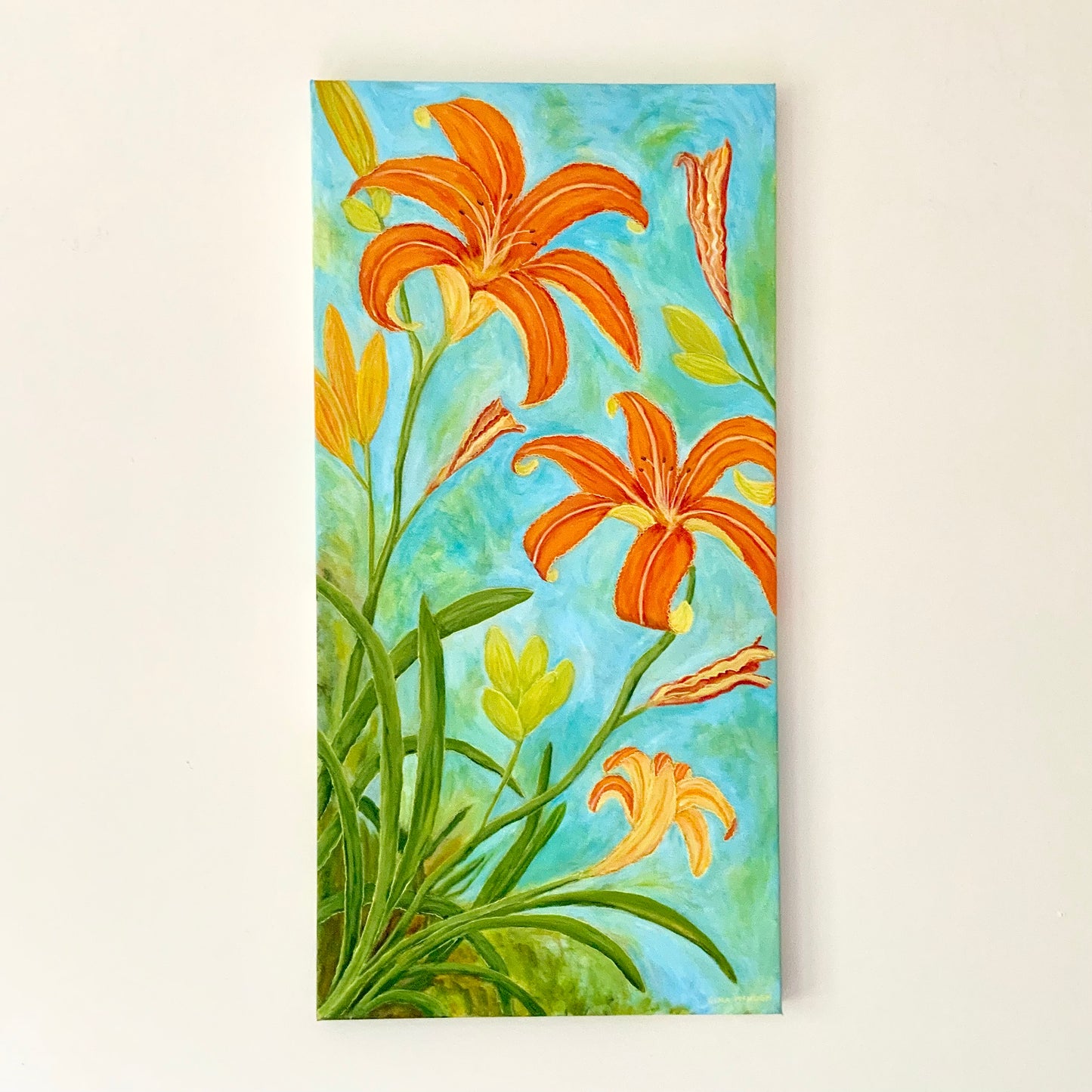 A vertical canvas painting of vibrant orange lilies and green foliage against a light blue and green textured background, displayed on a warm off-white wall.