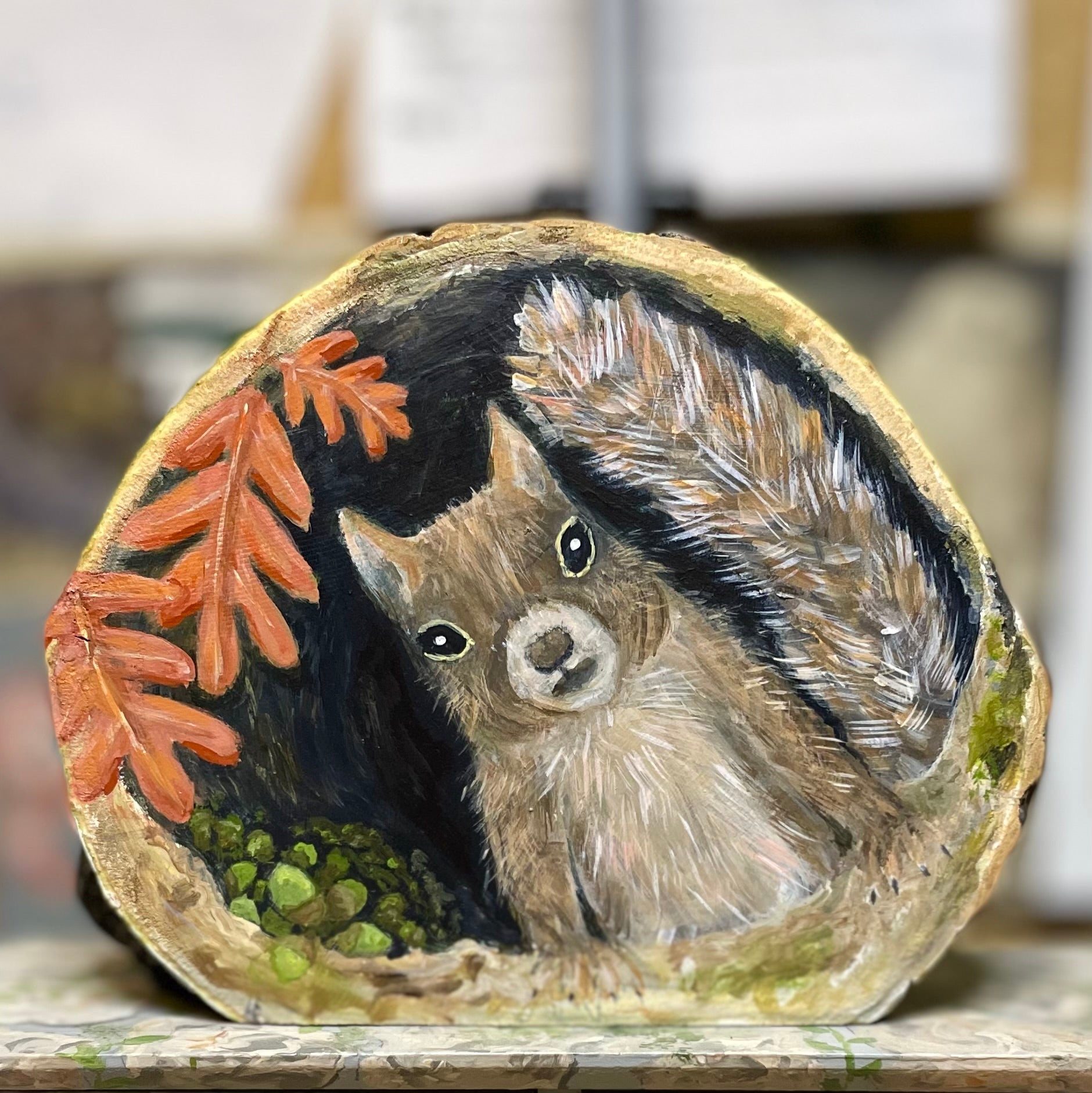 Painting of a squirrel nesting in a tree cavity with acorns and oak leaves on a freestanding aspen wood slice