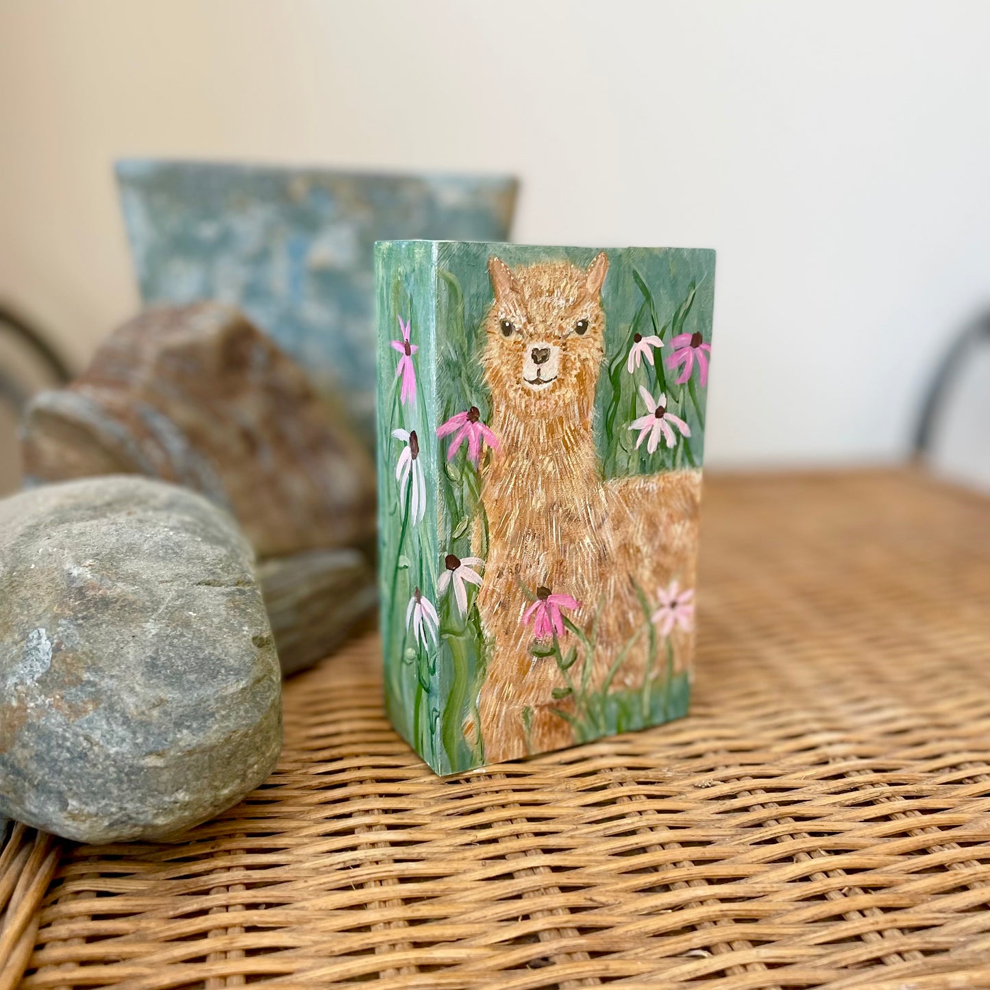 Small rectangular painting of a young alpaca in a field of flowers