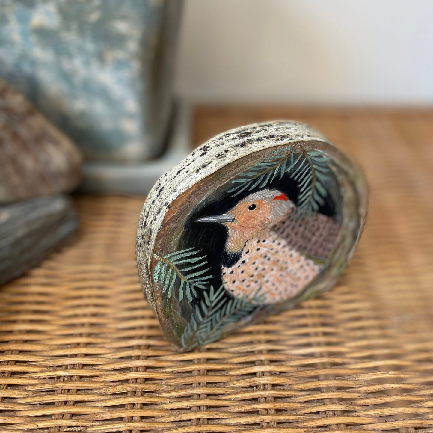 Painting of a northern flicker bird in a tree cavity with pine branches, on aspen wood slice with bark framing the outer edges