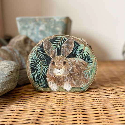 Snowshoe hare under pine branches painted on freestanding wood slice